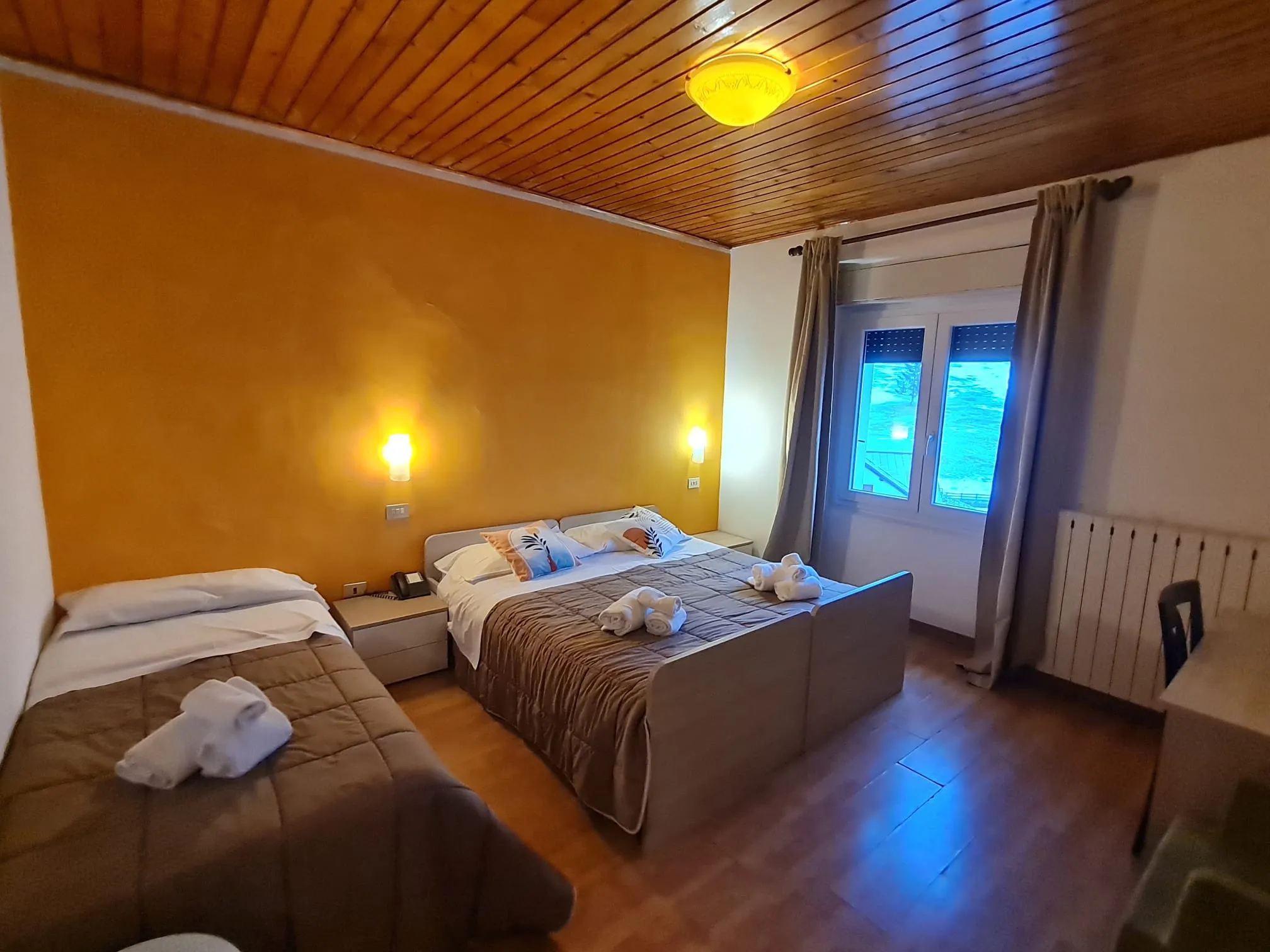 Camera tripla con letto matrimoniale e letto singolo, soffitto in legno e parete gialla
