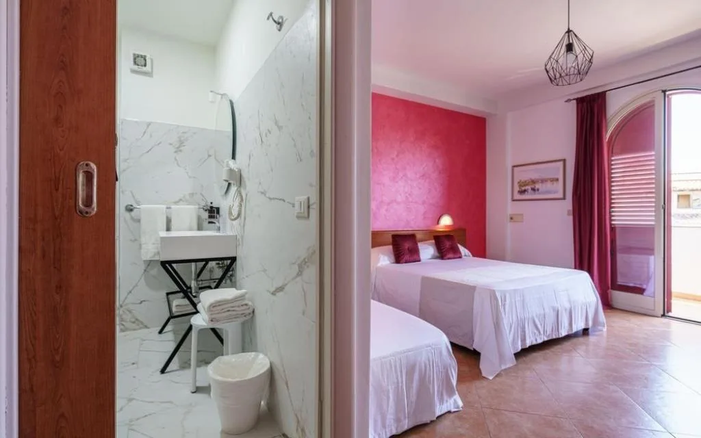 Camera con parete rosa, letto matrimoniale e bagno con doccia in marmo