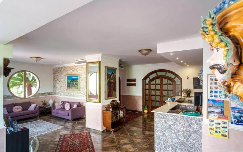 Hall dell'hotel con divani viola, decorazioni siciliane e reception