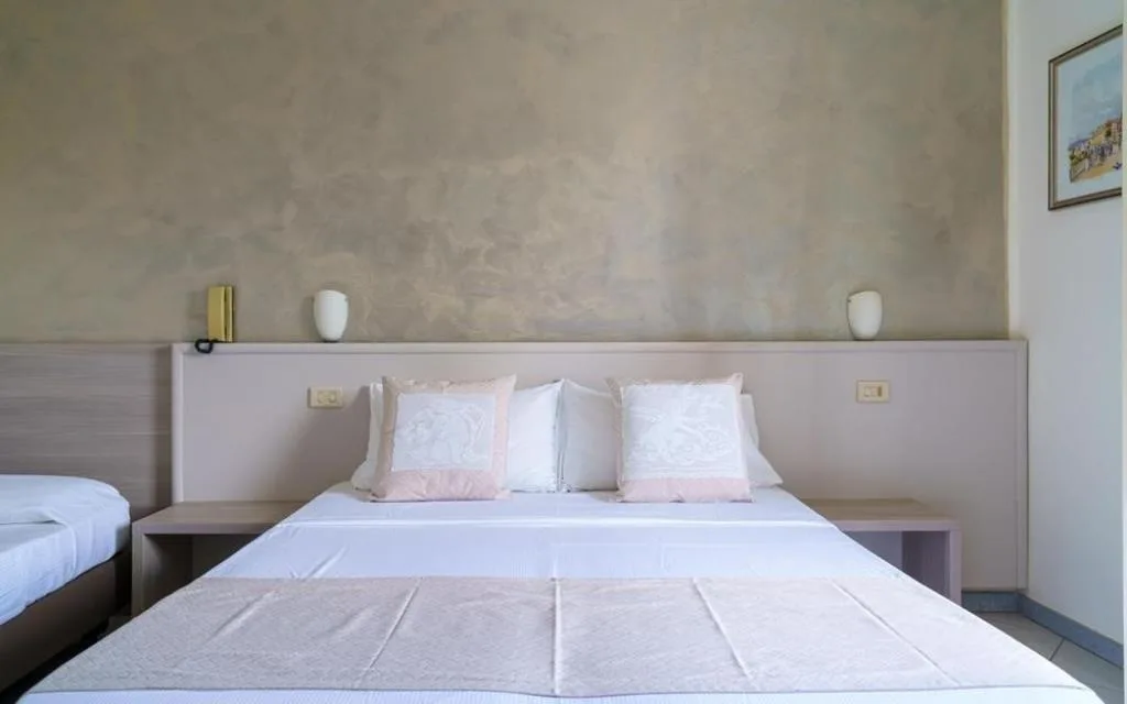 Dettaglio del letto con cuscini decorativi bianchi e testiera in legno