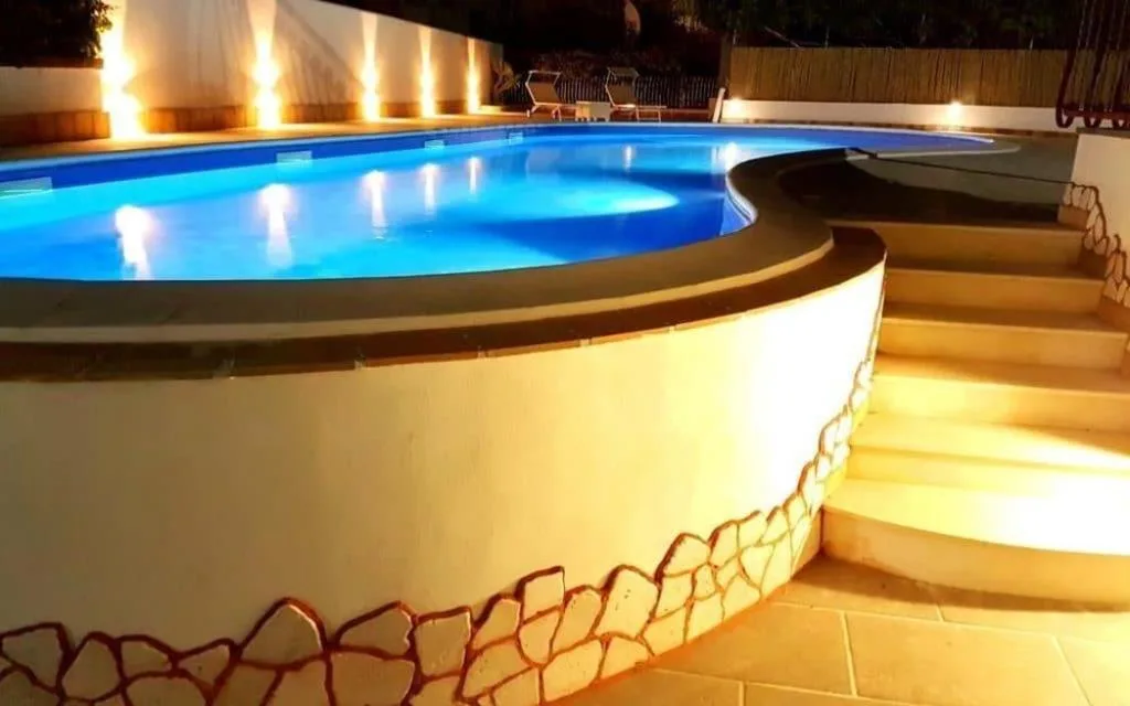 Piscina illuminata di notte con luci soffuse e scalinata in pietra