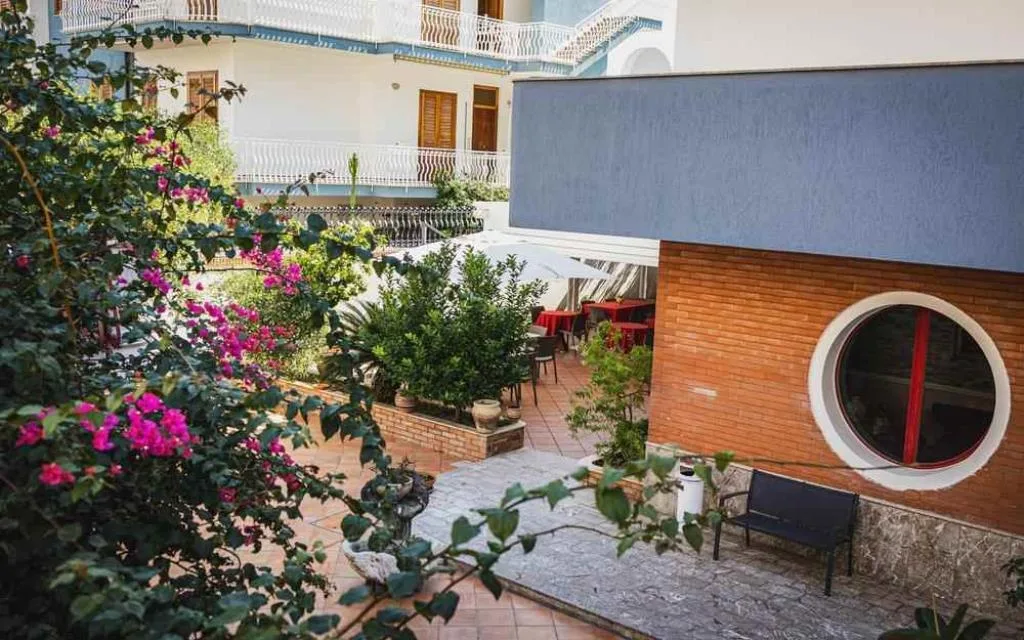 Cortile esterno con piante fiorite, bouganville e area relax con panchina