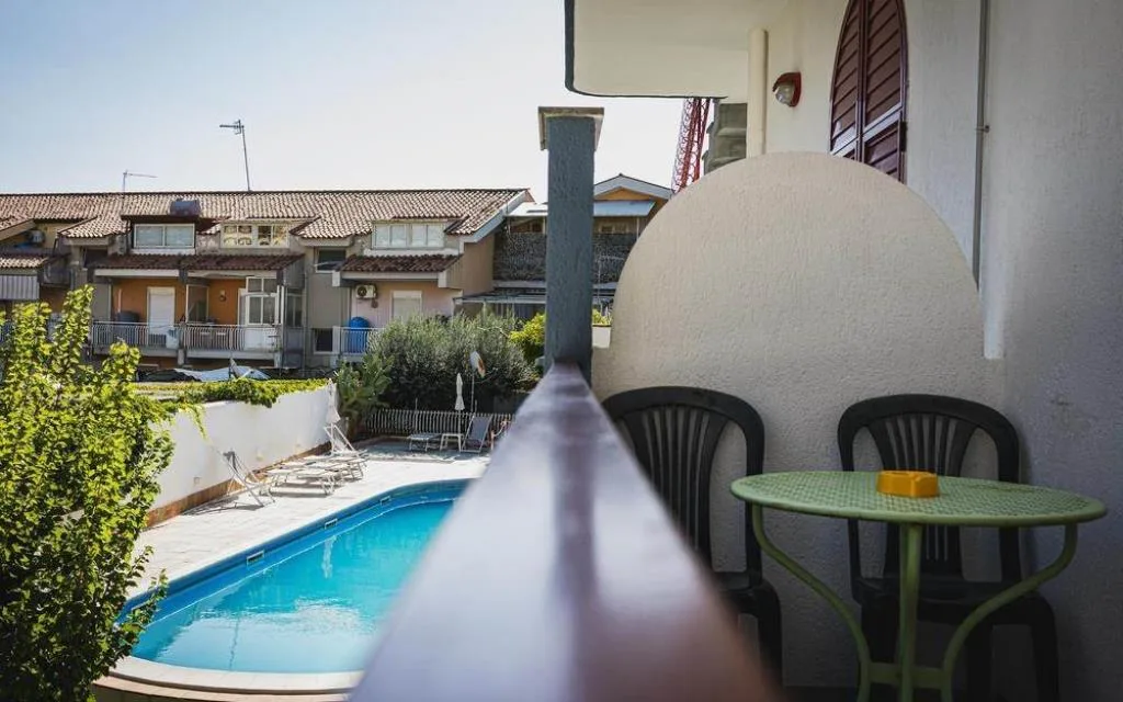 Balcone con tavolino verde e sedie affacciato sulla piscina