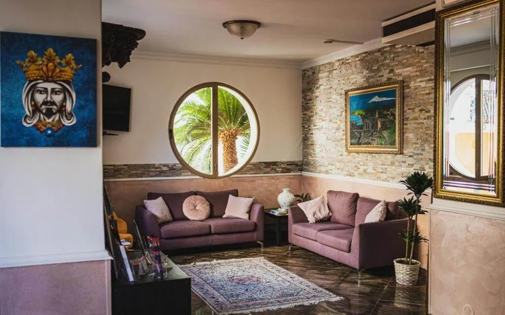 Salotto con divani viola, finestra rotonda e decorazione siciliana alla parete