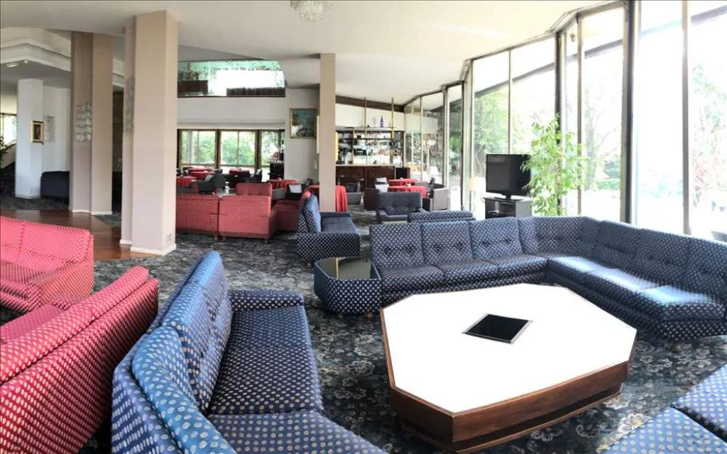Hall dell'hotel con divani rossi e blu e ampie vetrate sul giardino