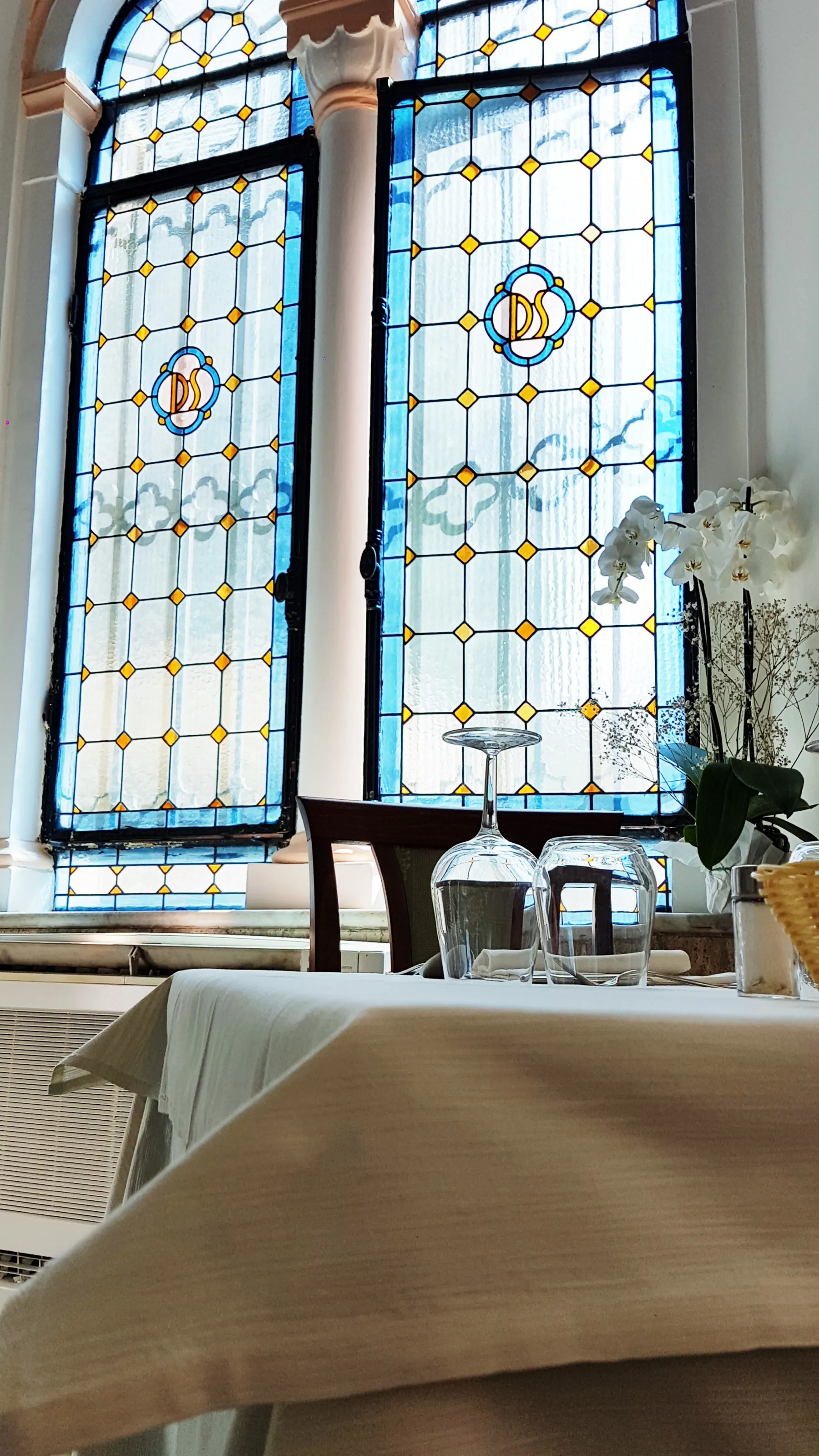 Sala ristorante con grandi vetrate decorate in stile liberty e tavoli apparecchiati