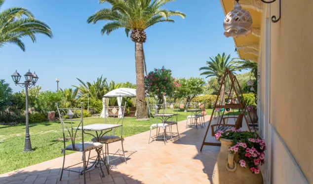 Terrazza esterna con tavolini, sedie e palme nel giardino fiorito