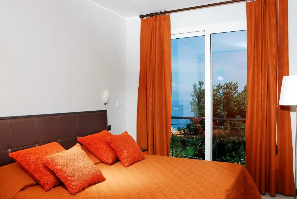 Camera da letto con copriletto e cuscini arancioni e finestra con vista mare