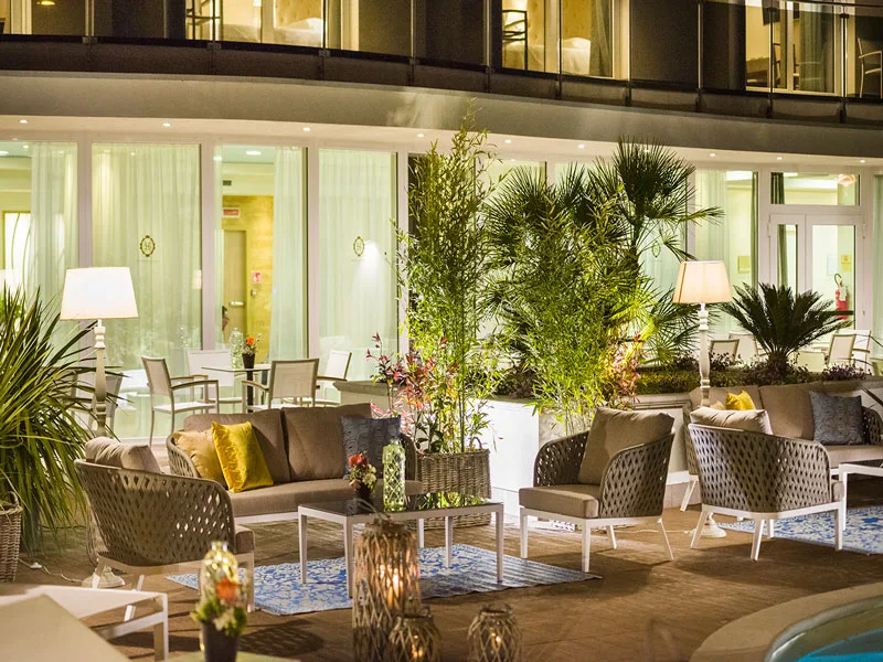 Area lounge esterna con divani, piante e illuminazione soffusa accanto alla piscina
