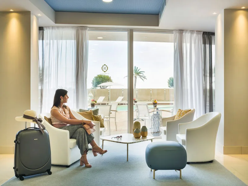 Donna seduta in poltrona con valigia nella hall dell'hotel affacciata sul terrazzo