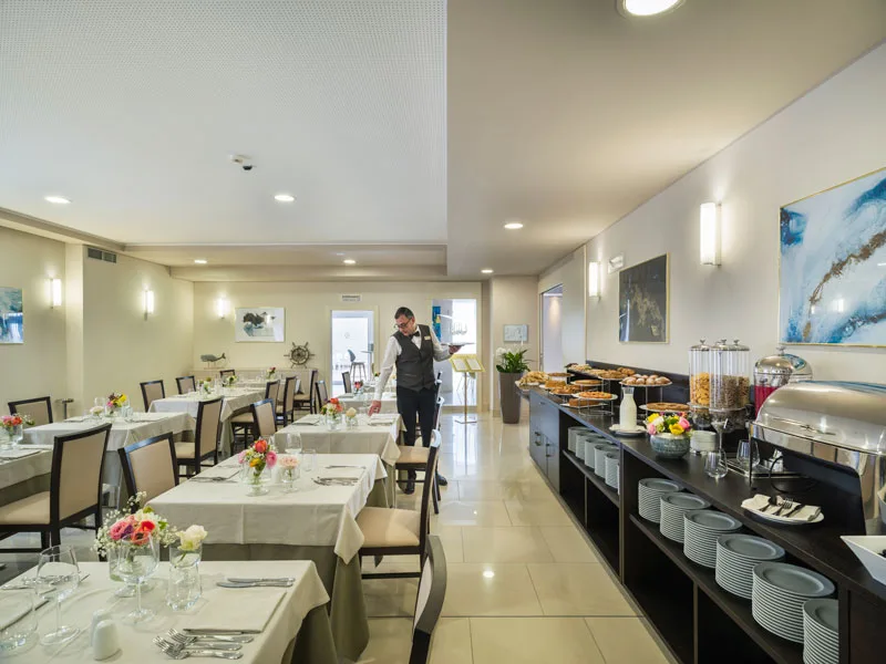 Sala colazioni dell'hotel con buffet, tavoli apparecchiati e cameriere