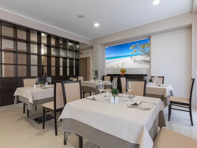 Sala ristorante elegante con tavoli apparecchiati e quadro di spiaggia tropicale