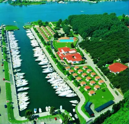 Veduta aerea di un villaggio turistico con porticciolo, barche, bungalow e piscina circondati dal verde