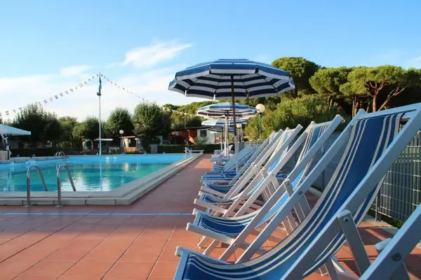 Lettini a righe blu e ombrelloni accanto a una piscina con pini sullo sfondo