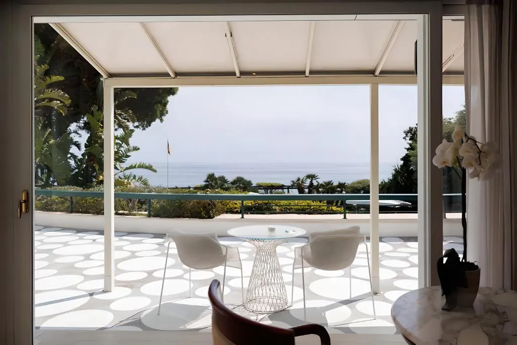 Terrazza con tavolo, sedie bianche e vista sul giardino e mare attraverso ampie vetrate