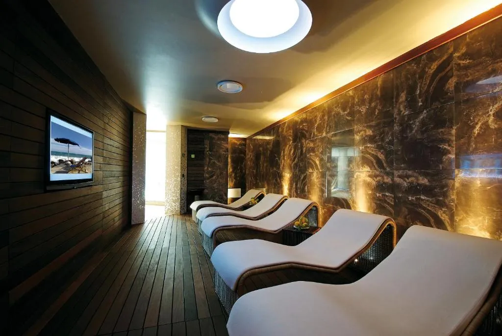 Area relax della spa con lettini sagomati, parete in marmo e schermo TV