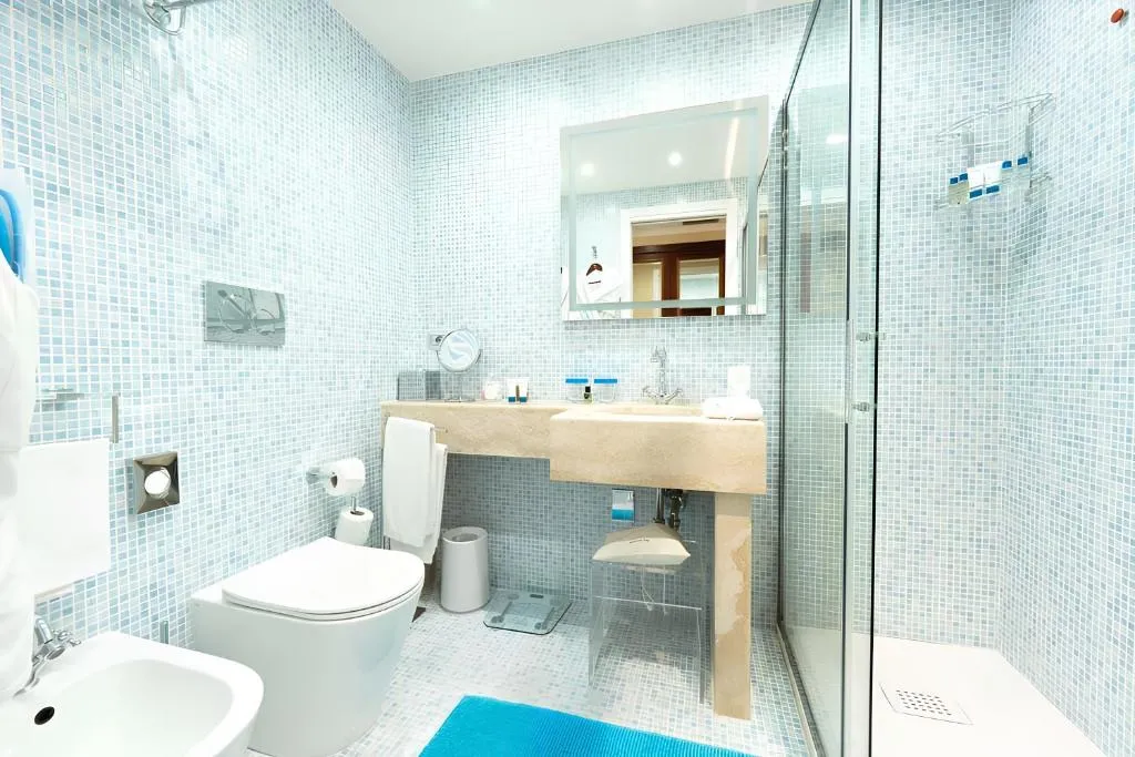 Bagno con rivestimento a mosaico azzurro, doccia in vetro e lavabo in pietra