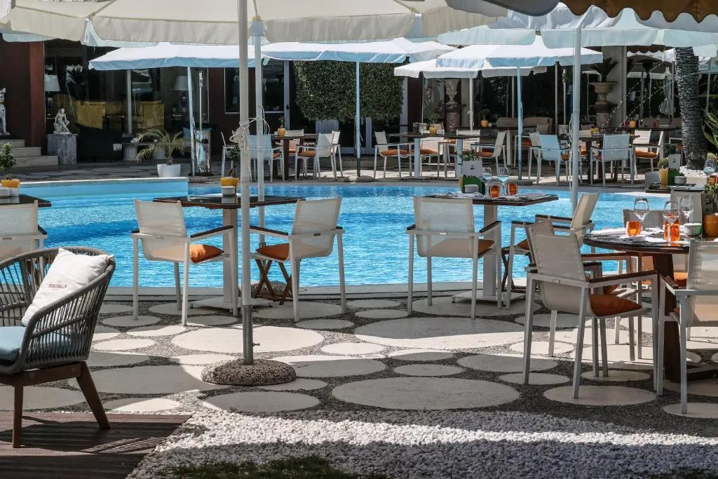 Area pranzo accanto alla piscina con tavoli, sedie bianche e ombrelloni