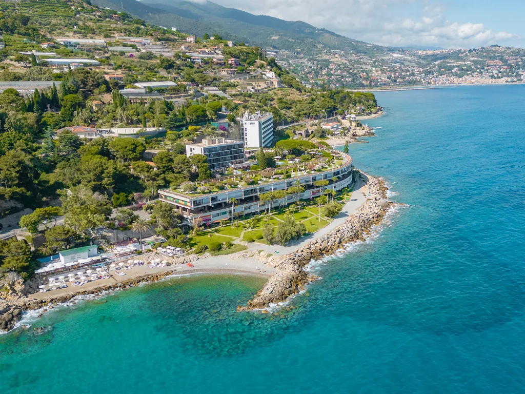 Panorama aereo dell'hotel sul promontorio con spiaggia e mare cristallino della riviera ligure