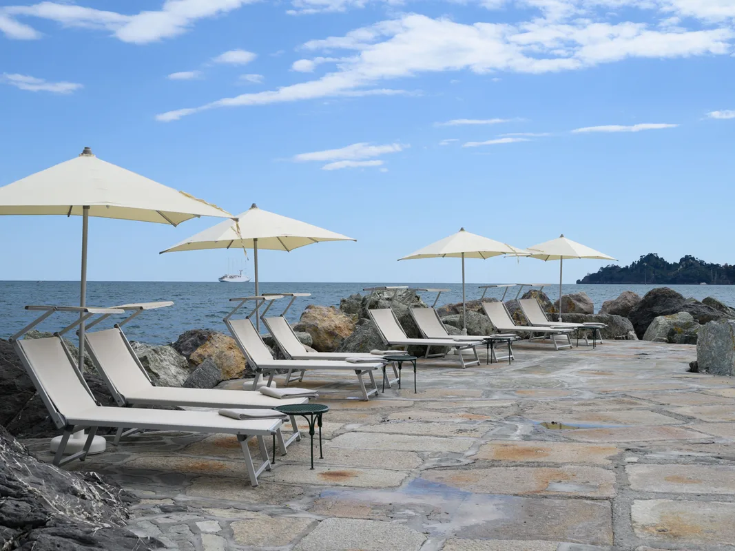 Lettini e ombrelloni su solarium in pietra a bordo mare con vista sulla costa
