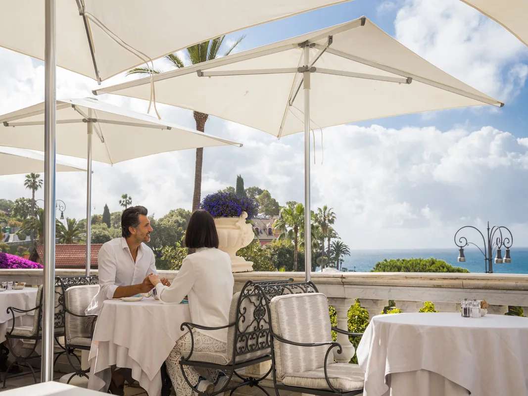 Coppia seduta a un tavolo sulla terrazza ombreggiata con vista sul mare e giardini