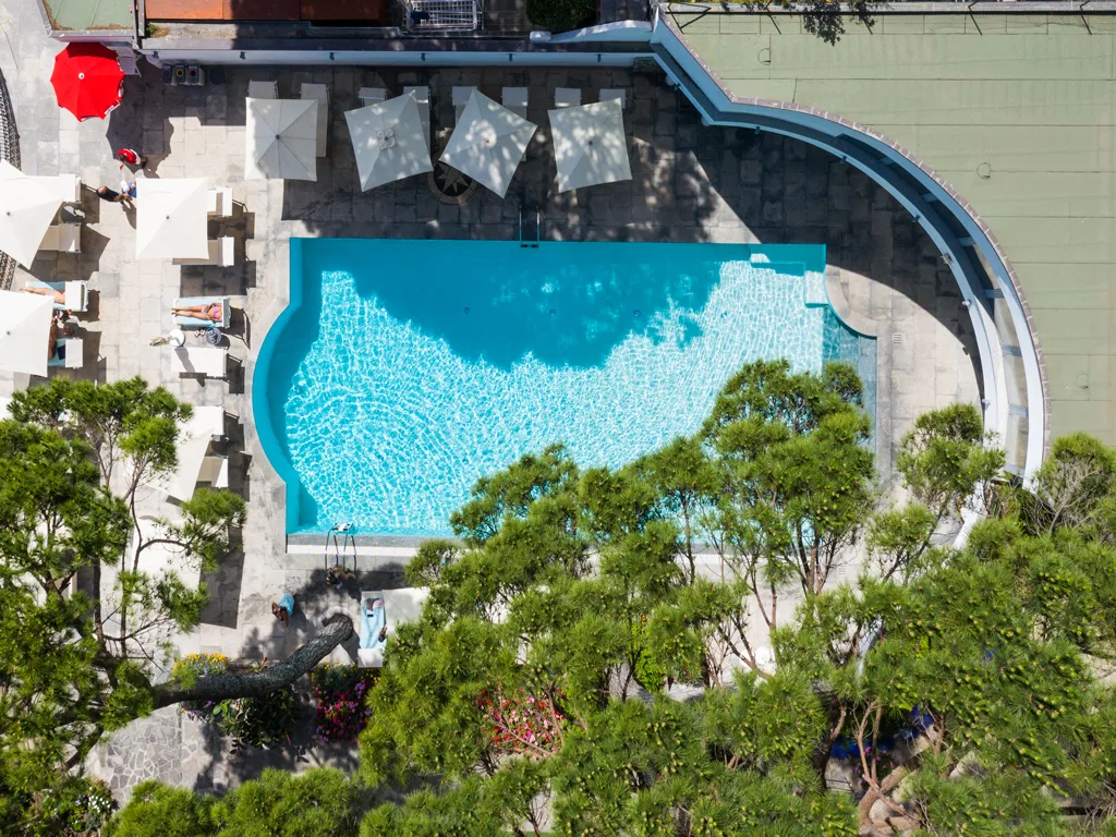 Vista aerea della piscina dell'hotel circondata da pini e vegetazione mediterranea