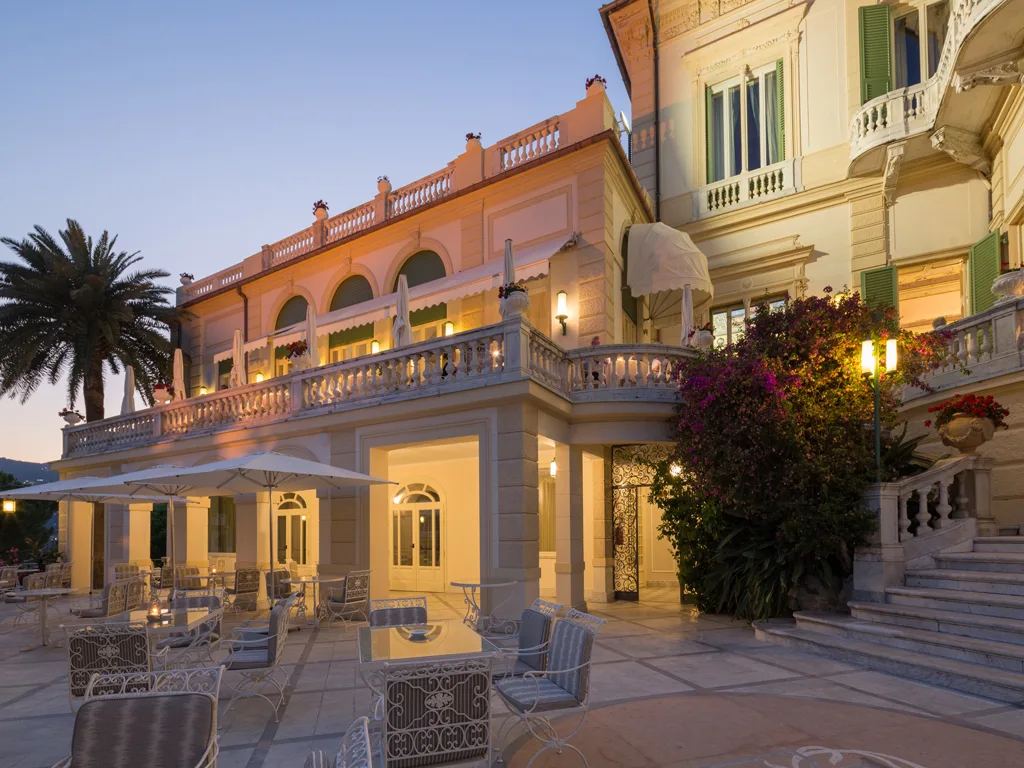 Terrazza esterna dell'hotel illuminata al tramonto con tavoli, palme e architettura storica