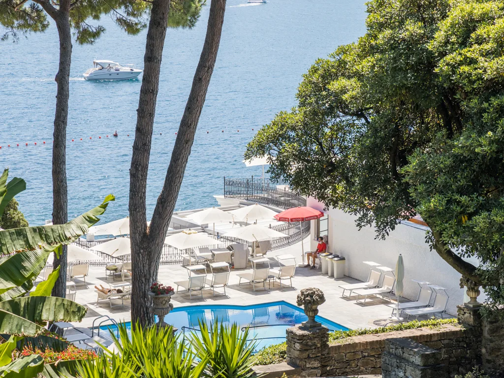 Vista sulla piscina e sul mare attraverso i pini con barca in navigazione