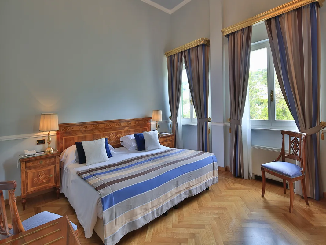 Camera con letto matrimoniale, arredi in legno intarsiato e finestre con vista