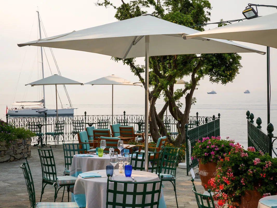 Terrazza ristorante a bordo mare al tramonto con tavoli apparecchiati e veliero