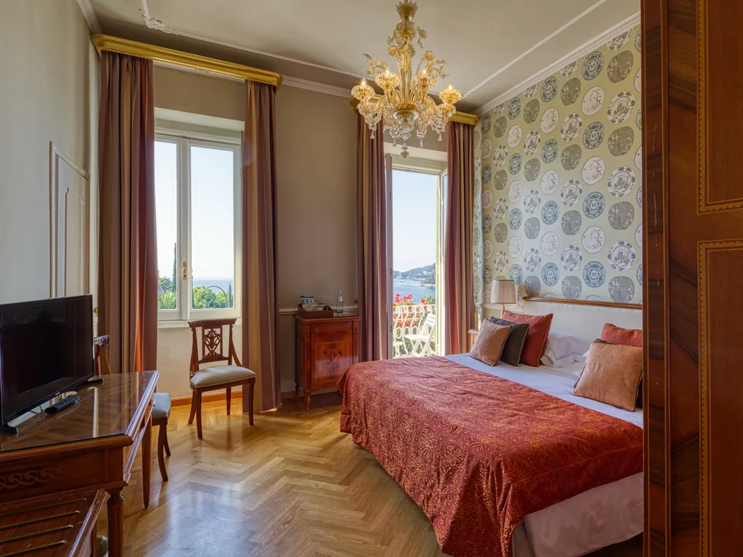 Camera matrimoniale classica con copriletto rosso, lampadario dorato e vista mare