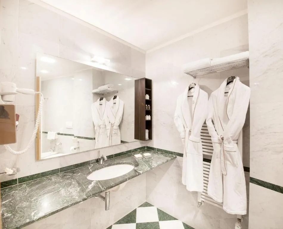 Bagno in marmo verde e bianco con accappatoi, specchio e lavabo