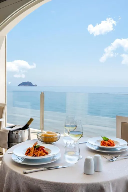 Tavolo apparecchiato con piatti di pasta e vino e vista mare sull'isola