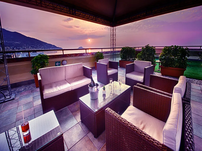 Terrazza lounge con divani in rattan e vista sul mare al tramonto
