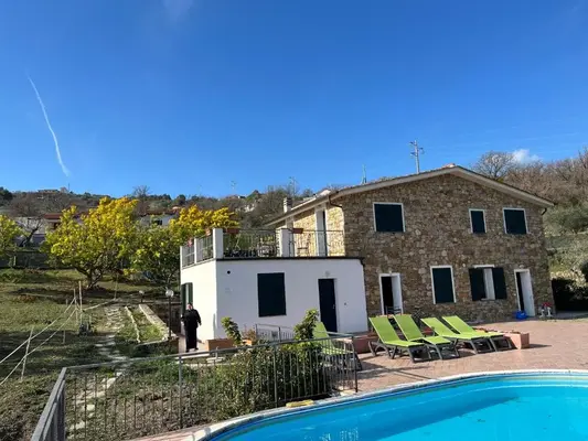 Casa in pietra con terrazza, lettini verdi e piscina nel giardino collinare
