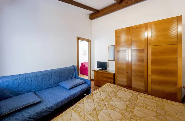 Camera con letto matrimoniale, divano blu, armadio in legno e TV