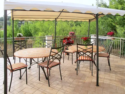 Terrazza esterna con gazebo bianco, tavoli rotondi e sedie a righe immersa nel verde