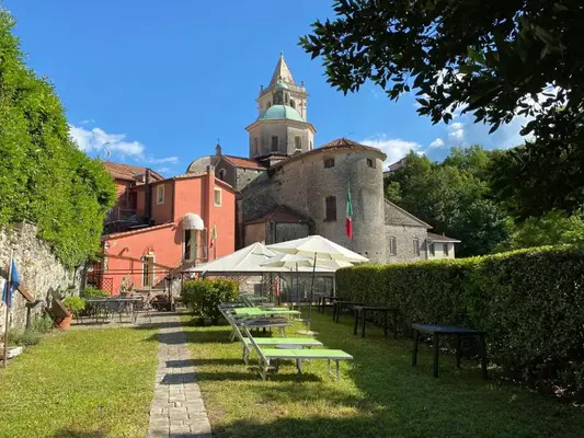 Giardino esterno con lettini, ombrelloni e vista sul campanile sotto cielo azzurro