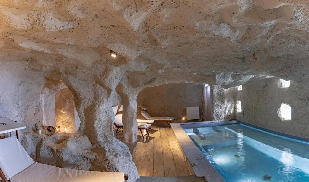 Piscina interna in ambiente in stile grotta con pareti in roccia e lettini relax