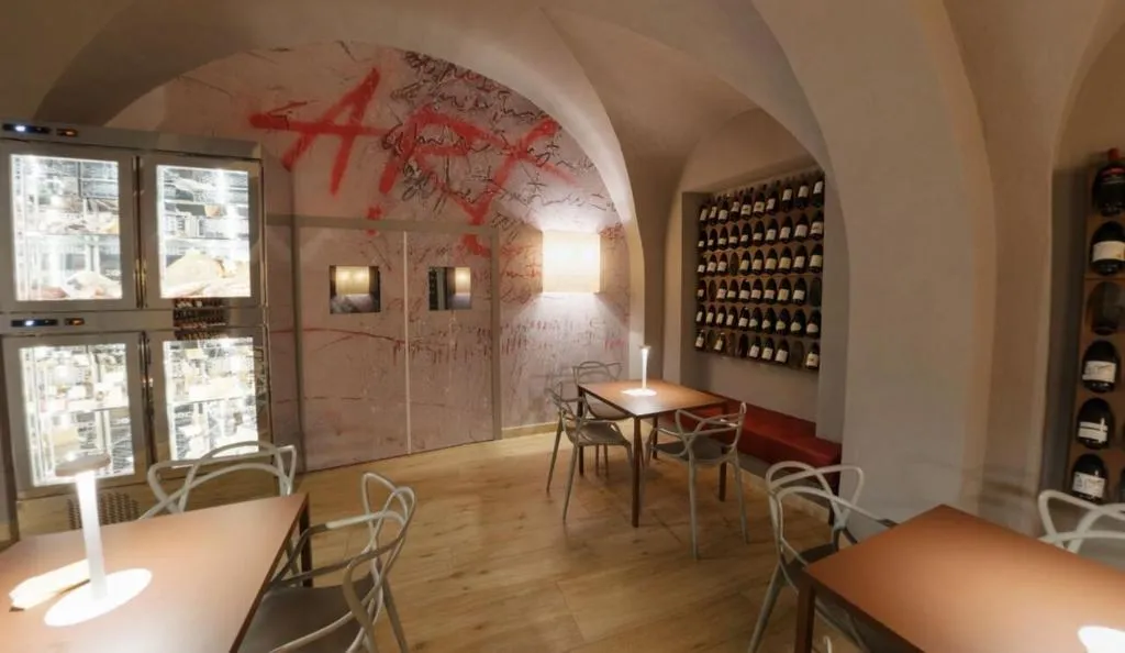 Cantina con tavoli, sedie di design e pareti decorate affiancate da espositori per vino