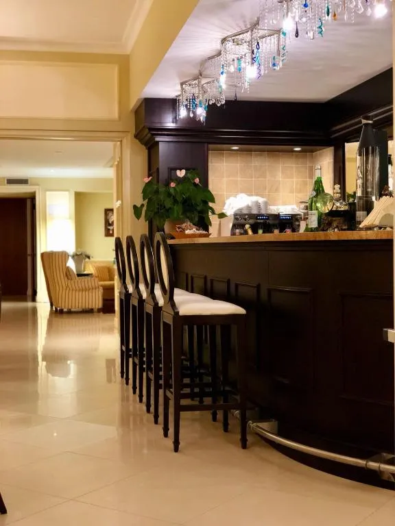 Bar dell'hotel con bancone in legno scuro, sgabelli e lampadario decorativo