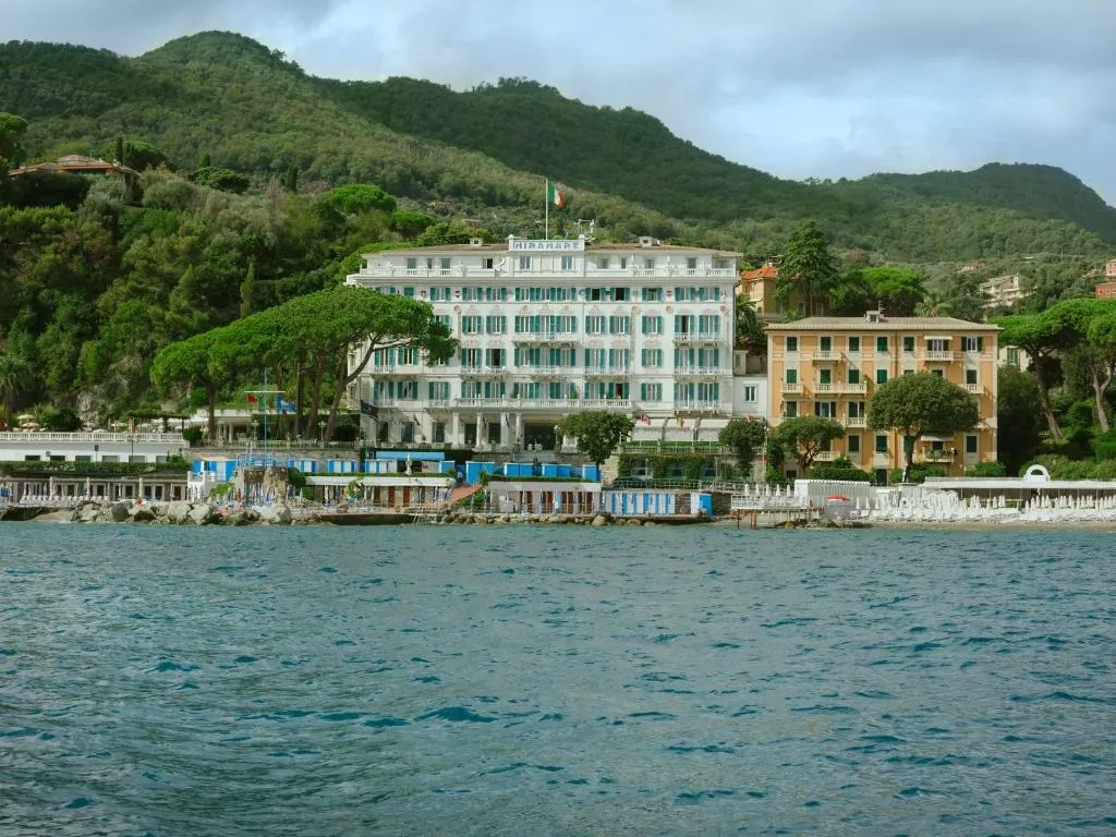 Vista dal mare dell'hotel storico fronte spiaggia incorniciato dalle colline verdeggianti