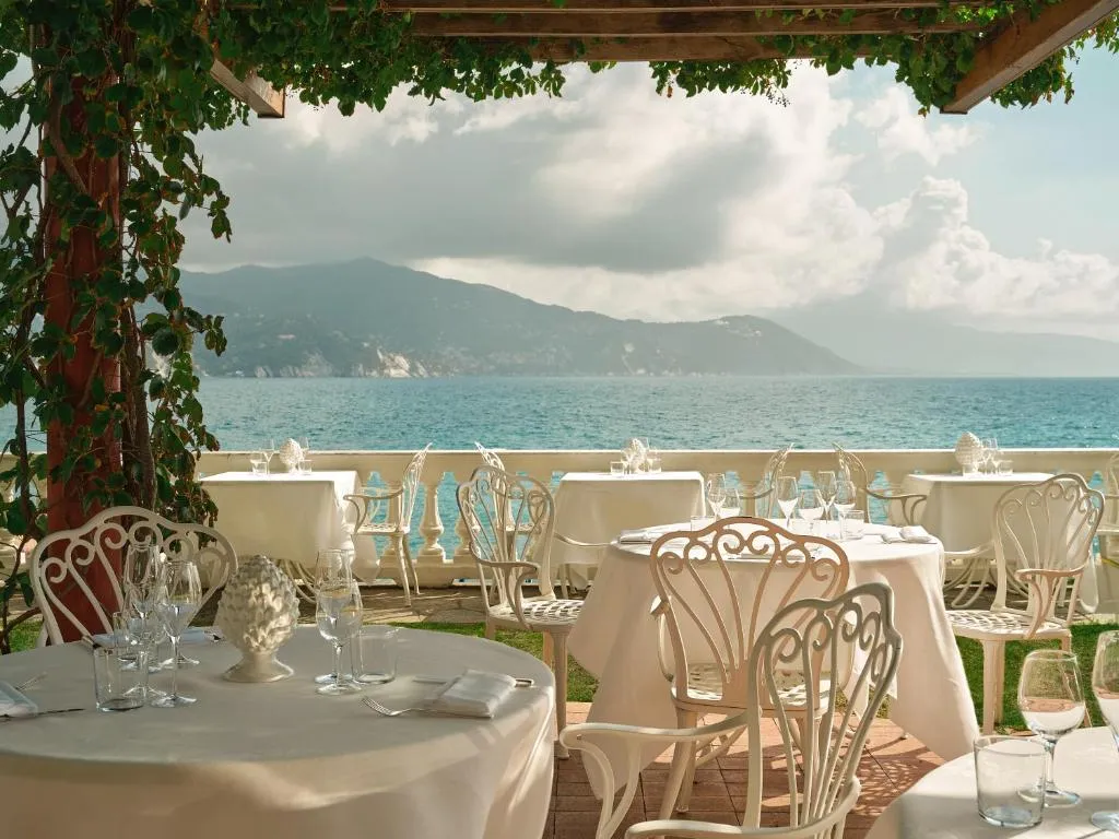 Terrazza ristorante con tavoli apparecchiati e pergolato affacciata sul mare e le colline