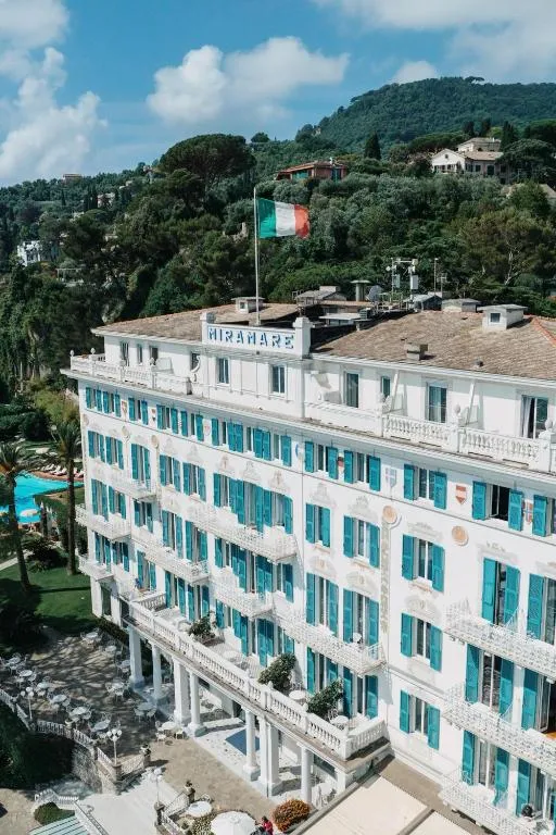 Facciata dell'hotel Miramare con persiane azzurre e bandiera italiana, immerso nel verde delle colline