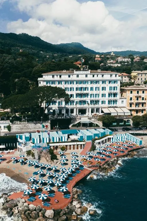 Veduta aerea dell'hotel storico bianco fronte mare con spiaggia attrezzata e ombrelloni