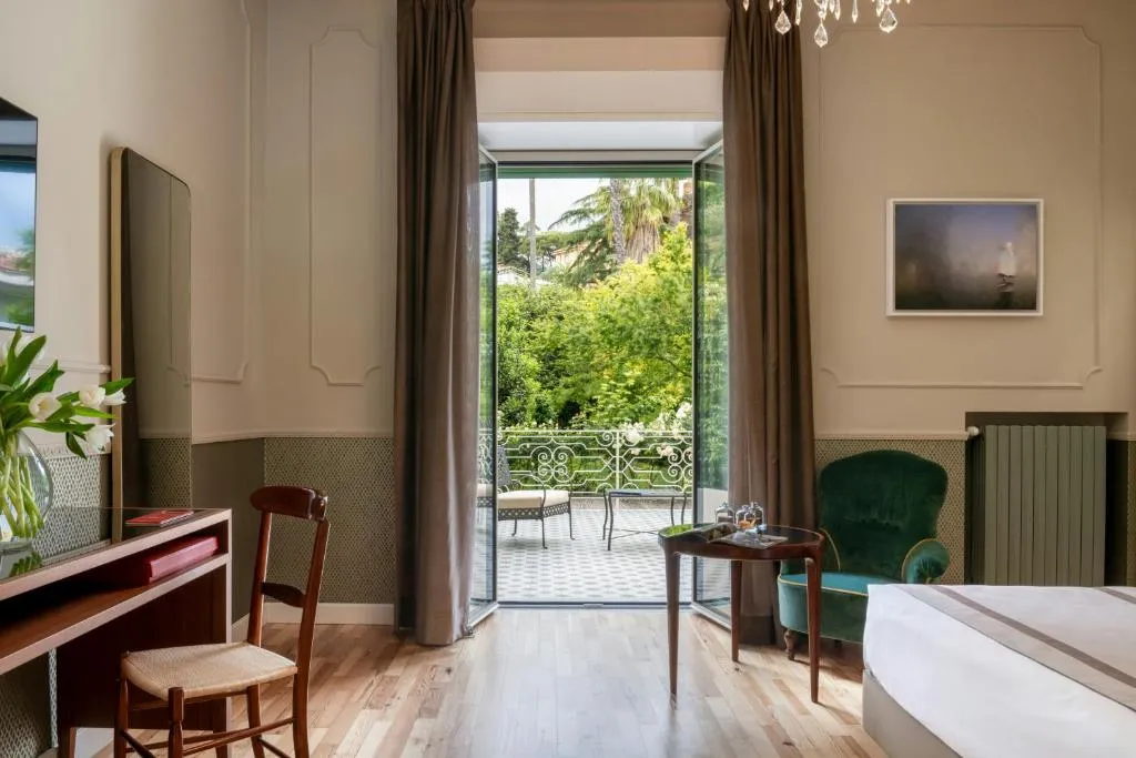 Camera elegante con scrivania, poltrona verde e ampia porta finestra che si apre sul terrazzo e il giardino