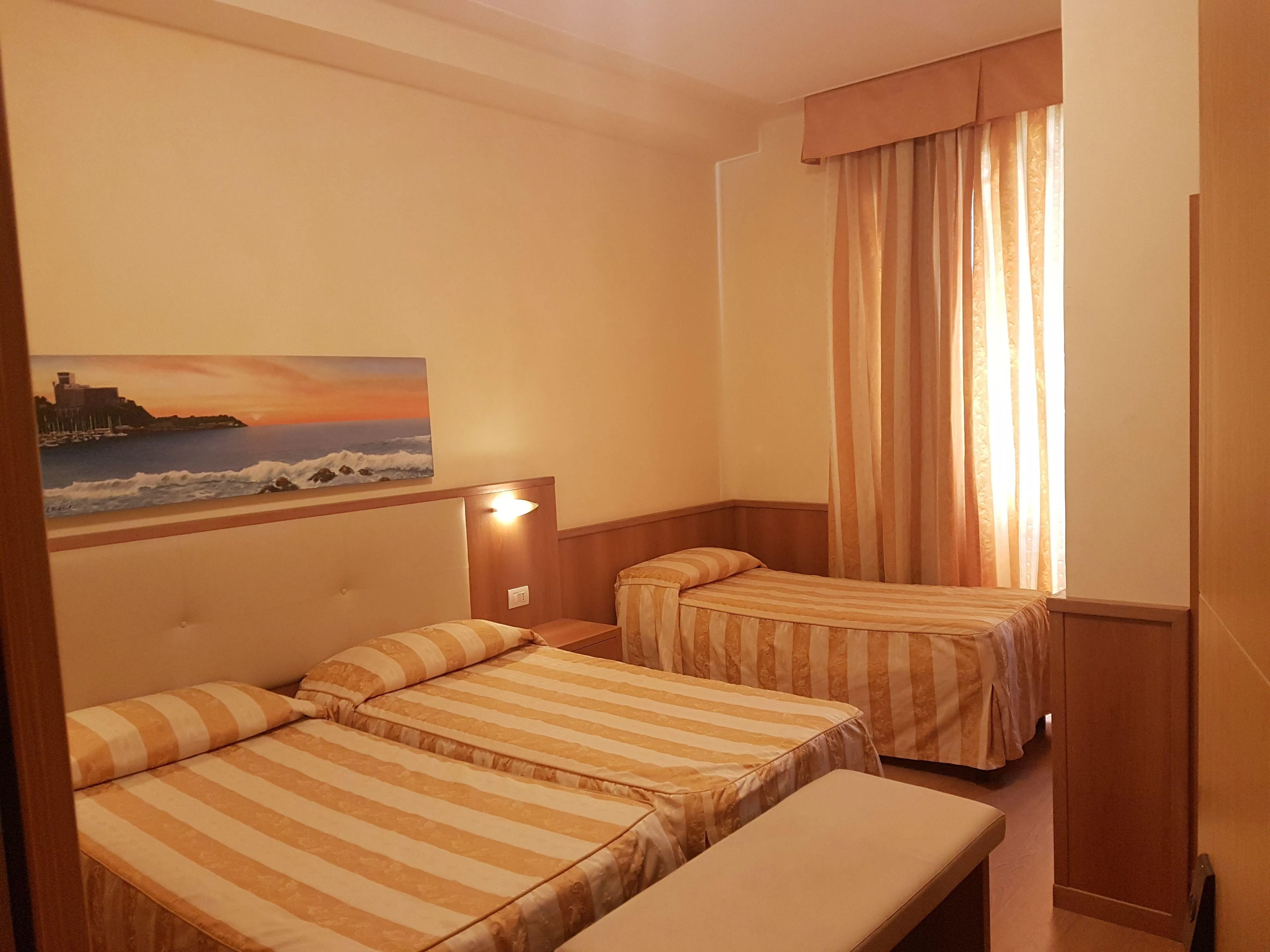 Camera tripla con due letti singoli, biancheria a righe e quadro con vista mare