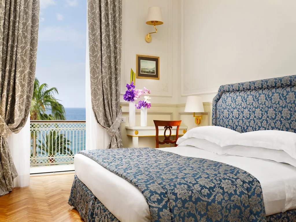 Camera elegante con testiera blu damascata e balcone affacciato sul mare tra le palme