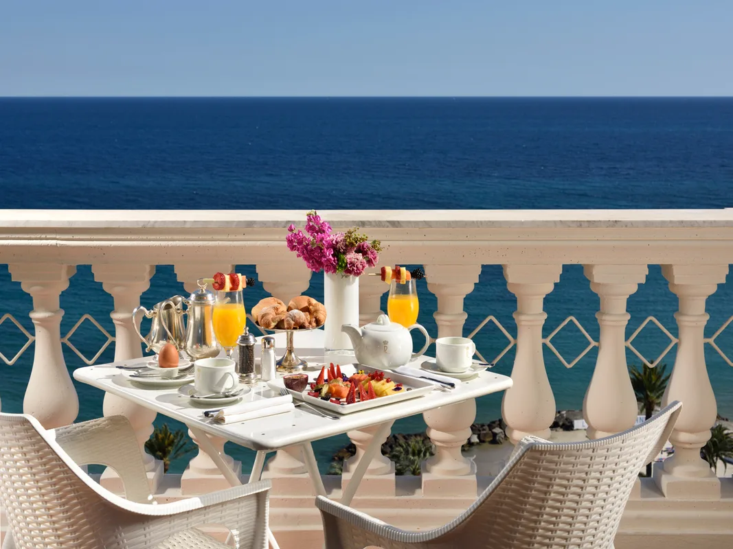 Colazione servita su tavolo in terrazza con balaustra affacciata sul mare blu
