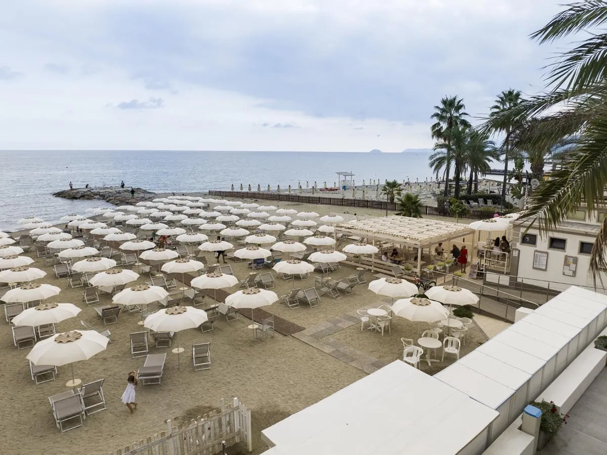 Spiaggia con ombrelloni bianchi, palme e vista sul mare in giornata nuvolosa